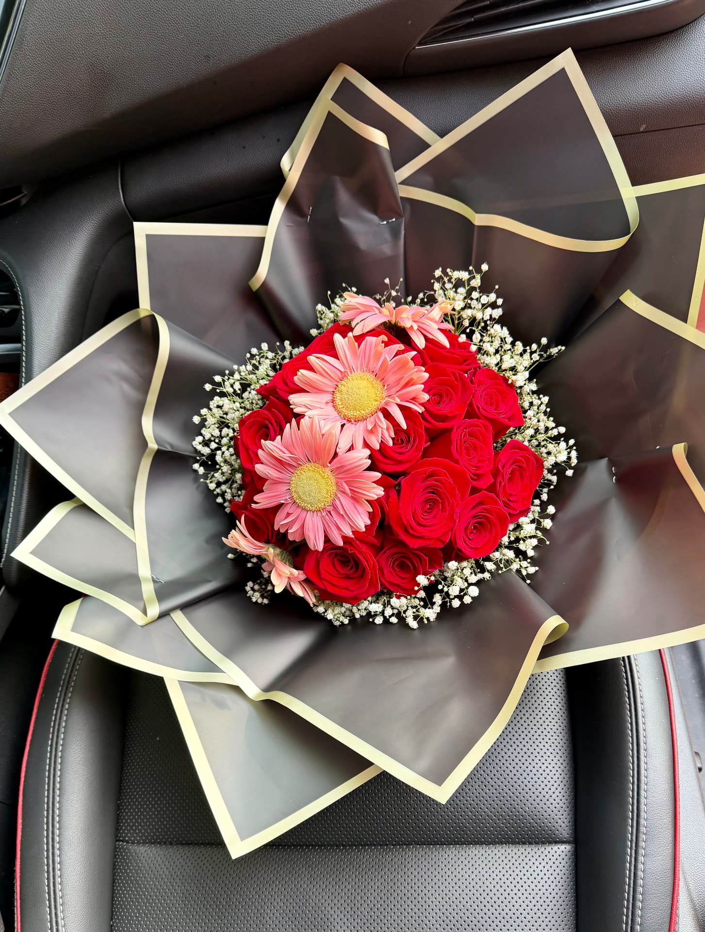 Red roses and pink gerbera daisies in black and gold wrap